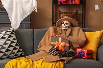 Scary Halloween skeleton in autumn clothes with gift box and tarantula sitting on sofa in living room