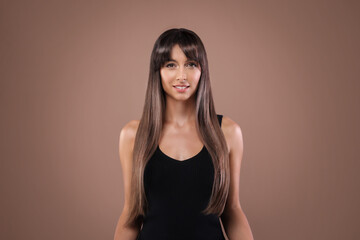Attractive woman with shiny straight hair on brown background. Professional hairstyling