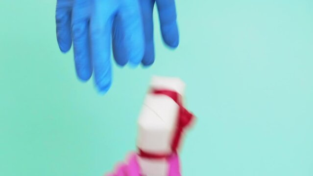 Vertical video. Pandemic gift. Coronavirus delivery. Set of 4 female hands in protective gloves teasing man with present in wrapped box isolated on blue background.