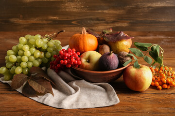 Bowl with different fresh fruits, pumpkin and berries on wooden background