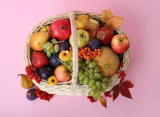 Wicker basket with different fresh fruits on pink background