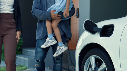 Progressive young parents and daughter living in a home with an electric vehicle and electronic vehicle charging station. Green and clean energy from electric vehicles for healthy environment. - Powered by Adobe