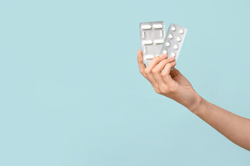 Female hand with pills in blister packs on blue background, closeup