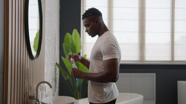 African American man cleaning teeth rinse with dental care product mouth hygiene at bathroom rinsing with antibacterial mouthwash fresh breath gargling liquid oral refreshment morning daily routine