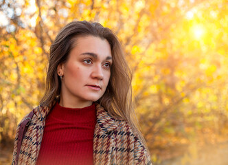 Portrait of a beautiful young woman in an autumn park in the sunshine
