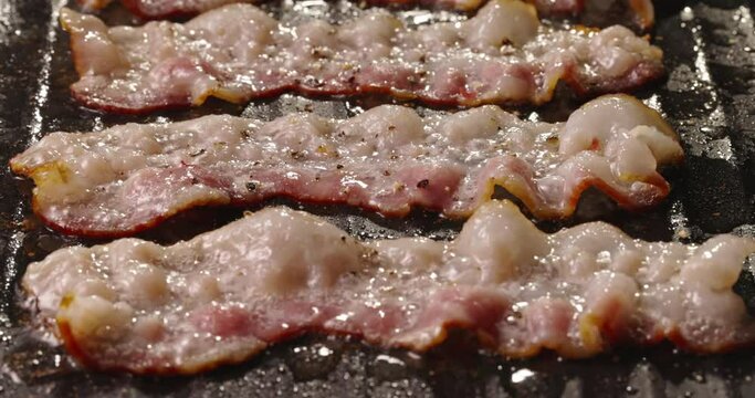 Frying halal beef bacon in pan side view close up. Bacon can be enjoyed in moderation as part of balanced diet. Process of frying bacon in pan. Meat bubbling in hot fat. Fried to perfect. Cholesterol