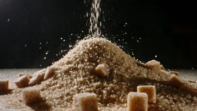 Loose and lump sugar. Brown cane sugar is poured onto table in heap. Dolly shot slow motion. Sensible sugar management is cornerstone of disease prevention, vital in avoiding obesity. Nutrition diet