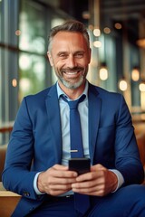 Smiling european mature man businessman holding smartphone sitting in an office working online on gadget