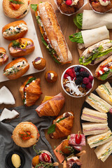 An assortment of baked goods and sandwiches are scattered across a wooden table.