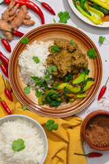 Freshly made chicken curry is seen from directly above. Ingredients including chilli and fresh turmeric surround the plate.