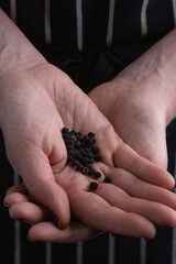 A woman's hand is seen holding a small pile of black peppercorns. 