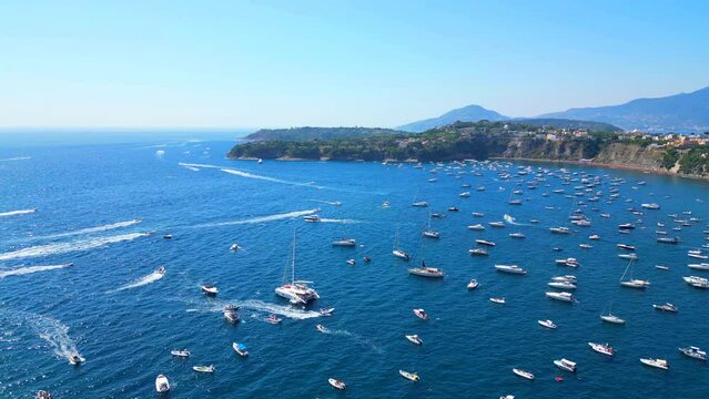 Lively aerial push-in from Panoramica sulla Corricella on Procida Island (Isola di Procida) with many white boats cruising the wavy blue Tyrrhenian Sea and leaving wakes amongst slopes and mountains