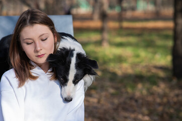 Caucasian woman hugging her dog Border Collie while sitting on a bench in autumn park.