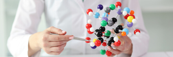 Woman in laboratory coat demonstrates model of molecule