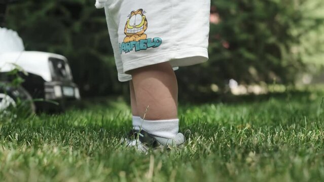 Close-up of the feet of a little boy in shorts and sandals walking on the grass on a sunny day.