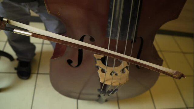 close up of a contrabass cello bass and a man wearing black sandals holding a stick to make the sound baroque era classical royal sounds played inside kingdom palace for important people man standing