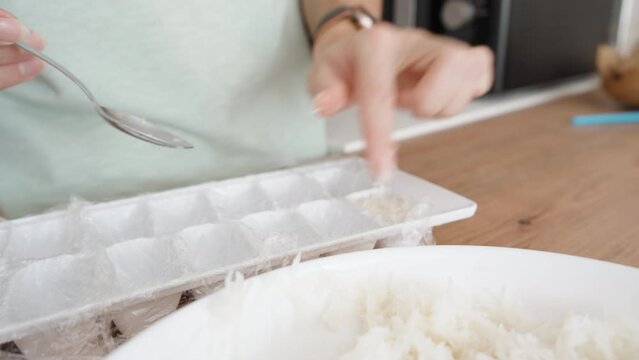 The Woman Places the Coconut Shreds into a Plastic Ice Tray, she is preparing sweet coconut candies.