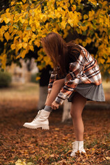 a young girl adjusts her shoes against the background of autumn foliage, autumn atmosphere, photo without a face