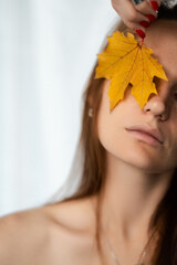 young girl holding an autumn yellow leaf to her face, close-up portrait