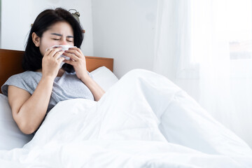asian woman feeling sick sneezing and have runny nose in bed hand holding tissue paper, allergic to dust mites or flu concept