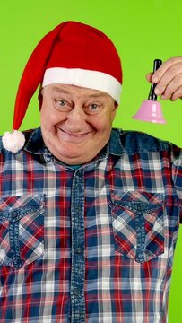 Joyful senior man in Santa hat rings Christmas jingle bell and laughs.