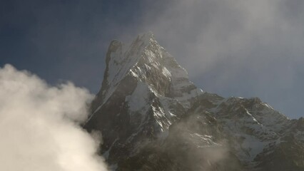 A view of Fishtail or Machhapuchhare Mountain in the morning light with the fog and clouds passing by in front of the snow covered peak.