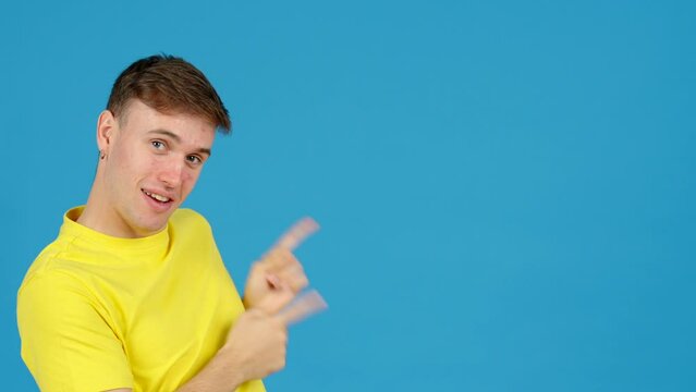 Young positive man pointing at blue copy space. Teenager boy showing message.