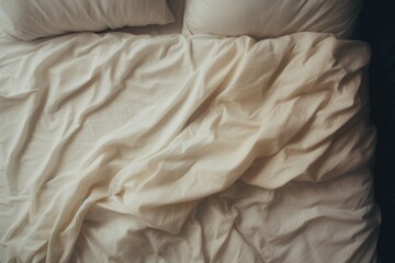 Top view of an unmade beige bed with a crumpled sheet, blanket and pillows