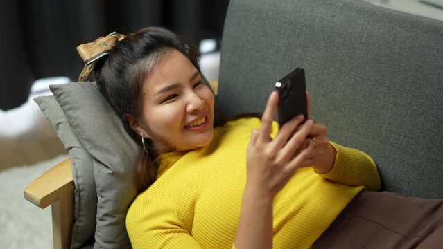 Asian women are Cute and beautiful women playing with a mobile phone, chatting, and watching movies online while relaxing on the sofa at home during the holidays.