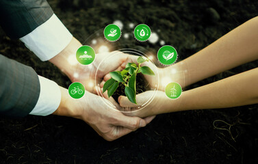 Businessman and little kid growing or nurturing plant together on fertile soil with eco friendly...