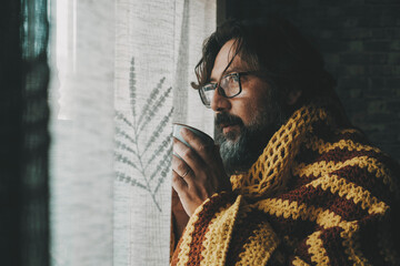 Side portrait of unhealthy man unhappy at home drinking medicine or coffee near the window looking...