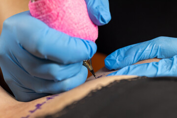 Needle tattoo machines inject a black ink into the skin of a woman. Tattoo art on body. Tattoo artist makes a tattoo woman on a arm, works in studio. close up view. High quality photo