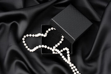White pearl necklace in a black box on black silk background