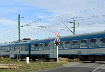 Obraz premium Red signal of semaphore and stop sign in front of railroad crossing with train passing.