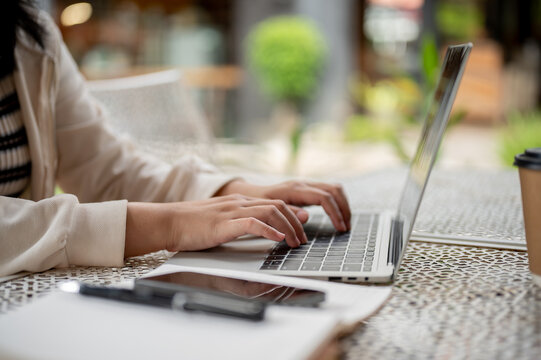Side view image of a woman using her laptop while sitting in the outdoor space of a coffee shop.