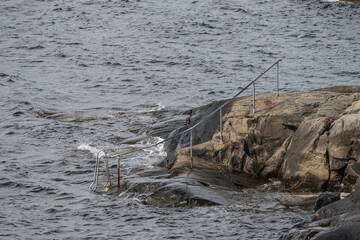 Metal railings and bathing ladder on cliffs at sea.