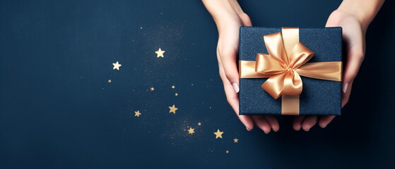 First person top view photo of female hands tying gold ribbon bow on craft paper Christmas gift box with copy space on blue background. Generative ai - obrazy, fototapety, plakaty