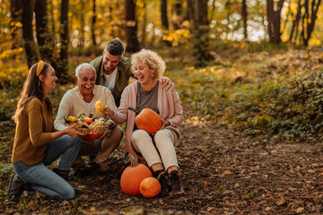 Two family generations sitting in the woods holding pumpkins