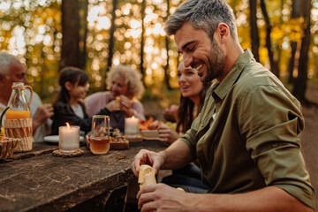 Father is breaking a baguette for his family during a picnic