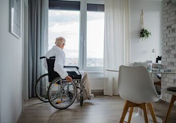 Senior man in a wheelchair spending time alone in apartment. Concept of loneliness and dependence of retired people. - obrazy, fototapety, plakaty