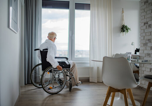 Senior man in a wheelchair spending time alone in apartment. Concept of loneliness and dependence of retired people.