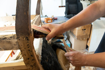 Upholsterer tightening a new strap on an old armchair, traditional craft skill to preserve antique furniture, copy space, selected focus - 666938778