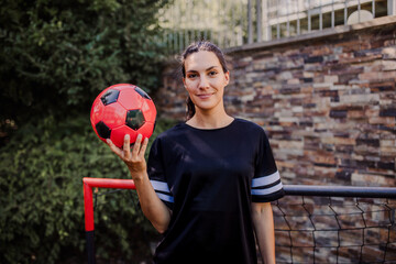 Beautiful female football player standing by football goal with ball in her hand. The woman plays soccer for relaxation. Concept of mental health and sport. © Halfpoint