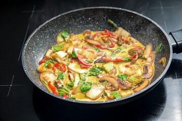 Vegetable Thai curry in a frying pan, ingredients like red bell pepper, mushroom, pak choi, seasoned with ginger, turmeric and onions, cooked in coconut milk, selected focus