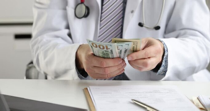 Male doctor sitting at table and counting dollar bill 4k movie slow motion. Corruption in medicine concept