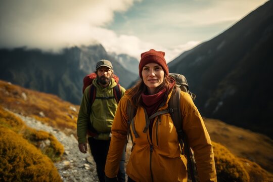 Happy young couple of tourists against the backdrop of stunning mountain landscape. Cheerful hikers in modern bright outfits with backpacks walking along mountain path. Active sports and travel.