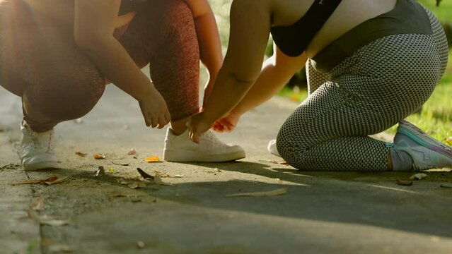 Plus-size lady overweight asian woman tie shoelaces prepared to run outdoors on a bright sunny day. Two young asian woman wearing sportswear training strong and good health and strength.