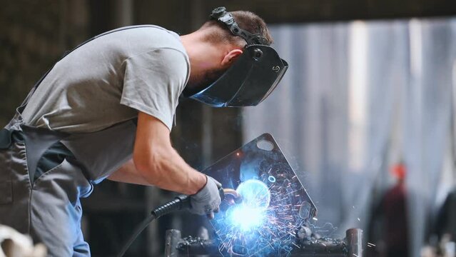The welder works at the factory collects a metal part. Working with Steel industry