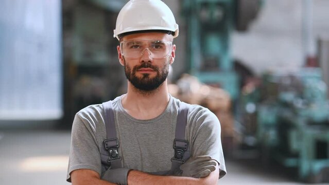 Portrait of a professional heavy industry engineer. Worker wearing protective uniform, goggles and helmet, smiling. In the background is a disoriented large industrial plant where welding sparks fly.
