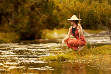 Woman with straw hat in middle of forest with river in background trees and nature warm colors, meditating in nature, traveling through east